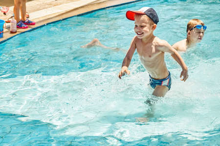 Cute brothers enjoy swimming in children pool at hotel territory. Preschooler in cap and schoolboy in goggles splash in clear water on vacationの写真素材