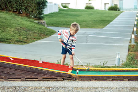 Boy enthusiastically plays mini golf on summer evening on the territory of the hotelの写真素材