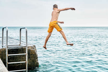 Moments of schoolboy jumping from stone pier with ladder into sea doing tricks in combined image...