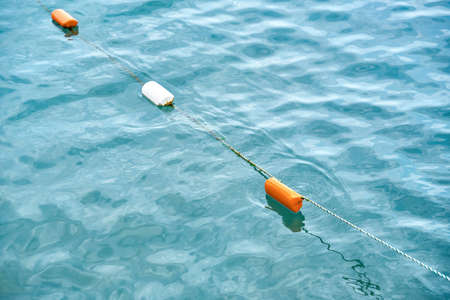 Installed bright red and white buoys waving on blue water surface. Equipped buoys show borderline of...