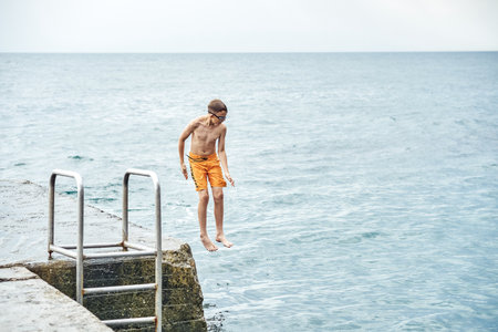 Moments of schoolboy jumping from stone pier with ladder into sea doing tricks in combined image sequenceの写真素材