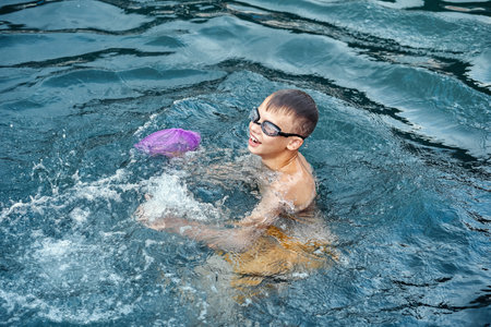 Schoolboy in swimming goggles enjoys holidays. Schoolkid swims in clear blue sea with smiling and...