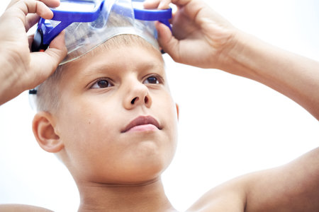 Teen schoolboy puts on blue goggles to swim exploring flora and fauna of sea. Teenager ready to enjoy summer holidays swimming underwaterの写真素材
