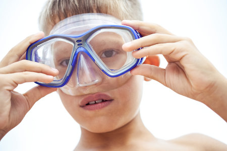 Teen schoolboy puts on blue goggles to swim exploring flora and fauna of sea. Teenager ready to enjoy summer holidays swimming underwaterの写真素材