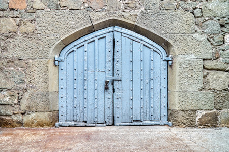 Blue wooden gate on wall surrounded by stones in medieval design hide mysterious things from arriving visitors. Exterior of medieval placeの写真素材