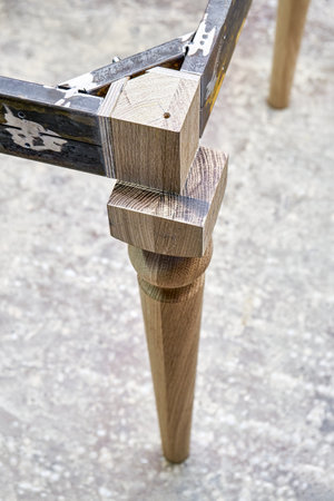Wooden carved leg of solid oak with metal table frame during manufacturing process of dining table in workshop close up viewの写真素材