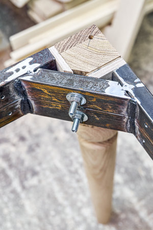Wooden carved leg of solid oak with metal table frame during manufacturing process of dining table in workshop close up viewの写真素材