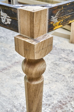 Wooden carved leg of solid oak with metal table frame during manufacturing process of dining table in workshop close up viewの写真素材