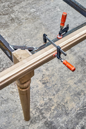 Wooden carved leg of solid oak with metal table frame during manufacturing process of dining table in workshop close up viewの写真素材