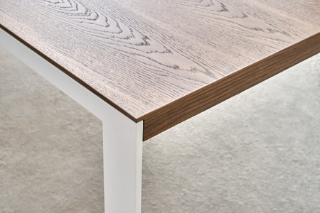 Minimalism style dining table with thin wooden table top of toned oak veneer on white metal legs closeupの写真素材