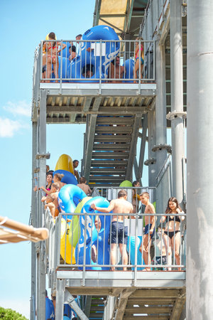 Gelendzhik, Russia - August 14 2021: People wait in line to ride slide on giant swimming pool slide attraction in aquapark at resort. Tourists stand on staircase landings with rubber ringsのeditorial素材