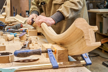 Carpenter sands bending wooden railing with sandpaper in workshop closeup. Senior master makes detail of spiral staircase for home interiorの写真素材