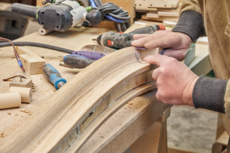 Carpenter sands bending wooden railing with sandpaper in workshop closeup. Senior master makes...