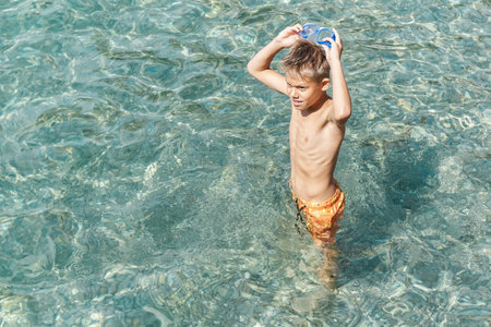 Teenager wearing swimming goggles enjoys summer holidays on sea beach. Excited teen blond boy prepares to swim underwater in gogglesの写真素材