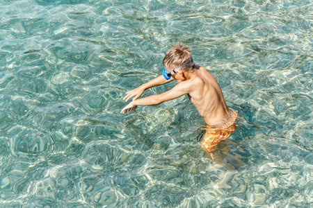 Junior school kid dives into deep transparent blue sea. Blond boy enjoying summer vacation at seaside resortの写真素材