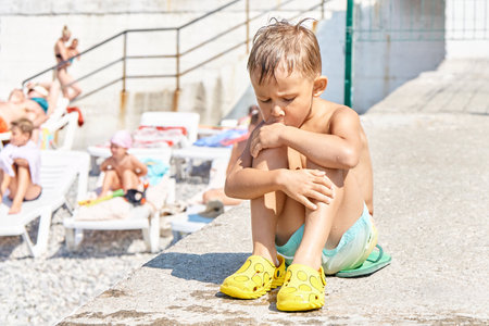 Preschooler boy sitting on sunny pier relaxes from swimming in sea. Kid with sad expression wants to spend more time in sunlit waterの写真素材