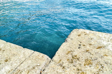 Gray concrete pier at blue sea water with small waves under bright sunlight on summer day in Portの写真素材