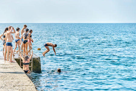 Gelendzhik, Russia - August 16 2021: Tourists jump from pier into water enjoying vacation on azure sea beach. Crowded pier with visitors arriving to azure sea resortのeditorial素材