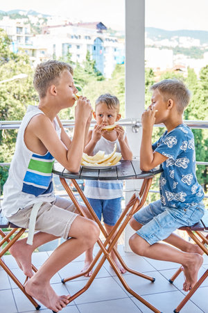 Junior school children and preschooler boy eating fresh melon on hotel terrace. Brothers spend together summer holiday at sea resortの写真素材