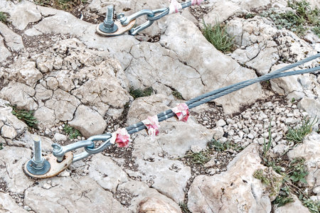 Fastening of suspension bridge braces into rock with large metal anchors closeup. Support equipment screwed into stones at mountain climbing parkの写真素材