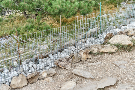 Gabion building process. Unfinished gabion building of rocks and metal mesh in nature park. Filling steel net basket with stones to make fence in garden. Border construction siteの写真素材