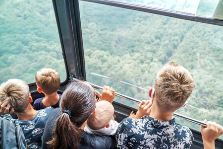 Mother with children ride funicular standing in cabin over green park. Large family with kids enjoy cable road trip together. Roperoad ridingの写真素材