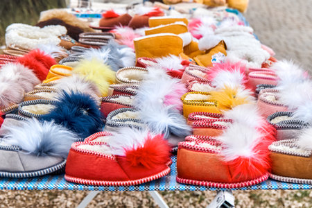 Warm woolen home shoes on craftsman display on city street closeup. Fur slippers and soft boots selling in town park. Craft shop with accessoriesの写真素材