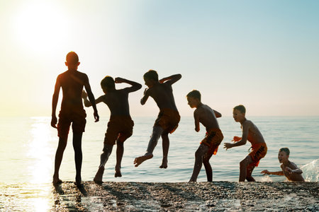 Sequence of jump. Moments of schoolboy jumping from stone pier into sea at sunrise doing tricks in combined image sequenceの写真素材