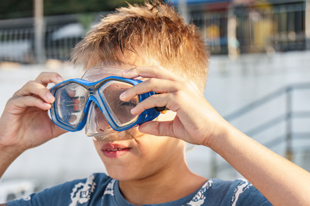 Boy puts on diving mask on beach at gentle sunset light closeup. Sportive child tries on equipment for underwater swimming at resort. Kid diverの写真素材
