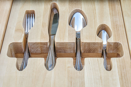 Shiny silverware in craved wooden tray in serving table drawer upper closeup view. Comfortable storage for cutlery keepingの写真素材