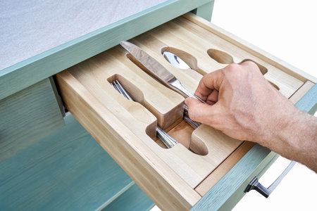 Man hand puts knife in craved wooden holder in kitchen cabinet drawer closeup. Person takes cutlery from storage tray. Home furnitureの写真素材