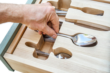Man hand puts spoon in craved wooden holder in kitchen cabinet drawer closeup. Person takes cutlery from storage tray. Home furnitureの写真素材