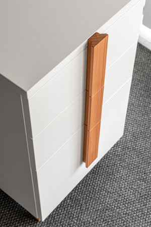 Minimalist white office chest of drawers with natural wooden brown handles and legs closeup view. Stylish furniture modelの写真素材