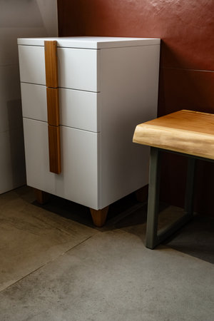 Live edge wooden bench with gray metal legs and white chest of drawers with wooden handles and legs in bathroom at low lightの写真素材