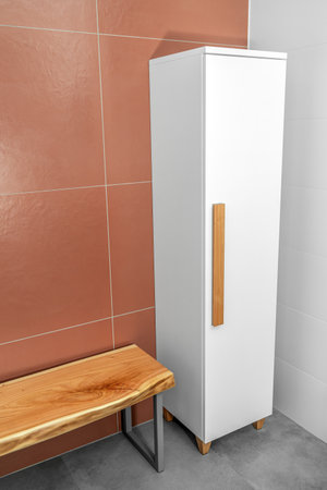 Live edge wooden bench with gray metal legs and white wardrobe with wooden handles and legs in bathroomの写真素材