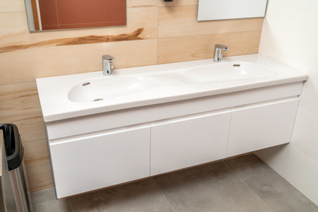 Wall mounted bathroom vanity cabinet with double white porcelain sink and silver sensor faucets in modern bathroom with concrete and wood tilesの写真素材
