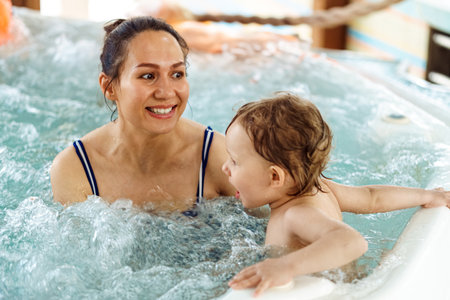 Cheerful woman with little child swim together in whirlpool bath. Happy mother and baby enjoy bathing in water with swirling bubbles at aquaparkの写真素材