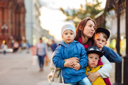 Busy mother with children group stands on city street. Woman and cute sons enjoys walk on town square. Large happy family with childrenの写真素材