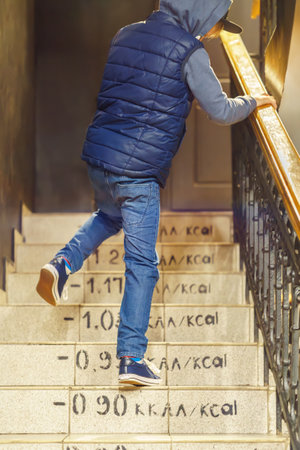 Boy wearing jeans and vest goes upstairs with burnt calorie marks on steps. Kid runs up steps to apartment. Playing childの写真素材