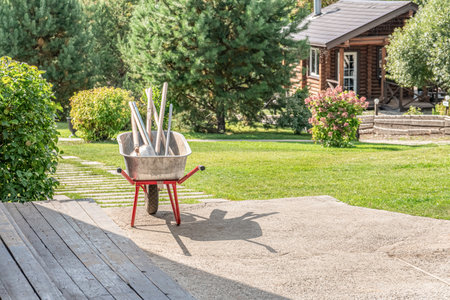 Metal cart with garden tools in sunny garden on cottage backyard. Trolley with hand instruments of gardener on lawn of country house. Country lifeの写真素材