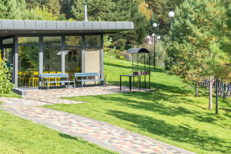 Guest house with glass walls and barbeque zone in yard at summer resort. Cafe building with outdoor grill equipment in garden. Place to restの写真素材