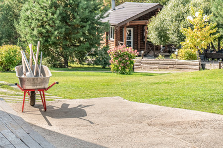 Metal cart with garden tools in sunny garden on cottage backyard. Trolley with hand instruments of gardener on lawn of country house. Country lifeの写真素材