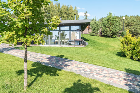 Guest house with glass walls and barbeque zone in yard at summer resort. Cafe building with outdoor grill equipment in garden. Place to restの写真素材