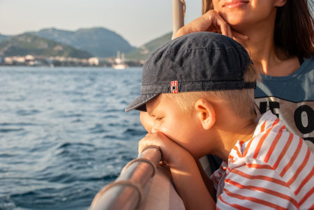 Cute toddler with mother enjoys boat trip sailing in sea past coast of Marmaris. Portrait of boy in sun-protective cap on vacation in Turkey closeupの写真素材