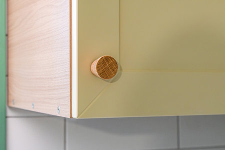 Wooden handle attached to yellow sleek kitchen cabinet with a simple design. Solid oak cabinet knob close up viewの写真素材