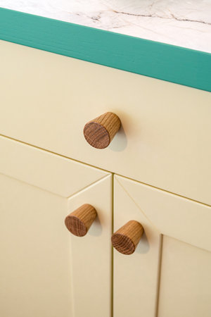 Wooden handles attached to yellow sleek kitchen cabinets with a simple design. Solid oak cabinet knobs close up viewの写真素材