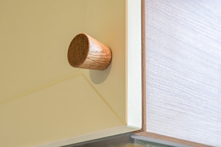 Wooden handle attached to yellow sleek kitchen cabinet with a simple design. Solid oak cabinet knob close up viewの写真素材