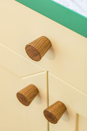 Wooden handles attached to yellow sleek kitchen cabinets with a simple design. Solid oak cabinet knobs close up viewの写真素材