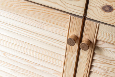 Wooden louvered doors with wooden knob handles close-up. Louvered doors of outdoor kitchen are made from light pine wood with natural grain patternの写真素材