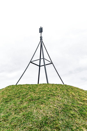 Metal structure on lush green hilltop with cloudy white sky in background, highest point in area